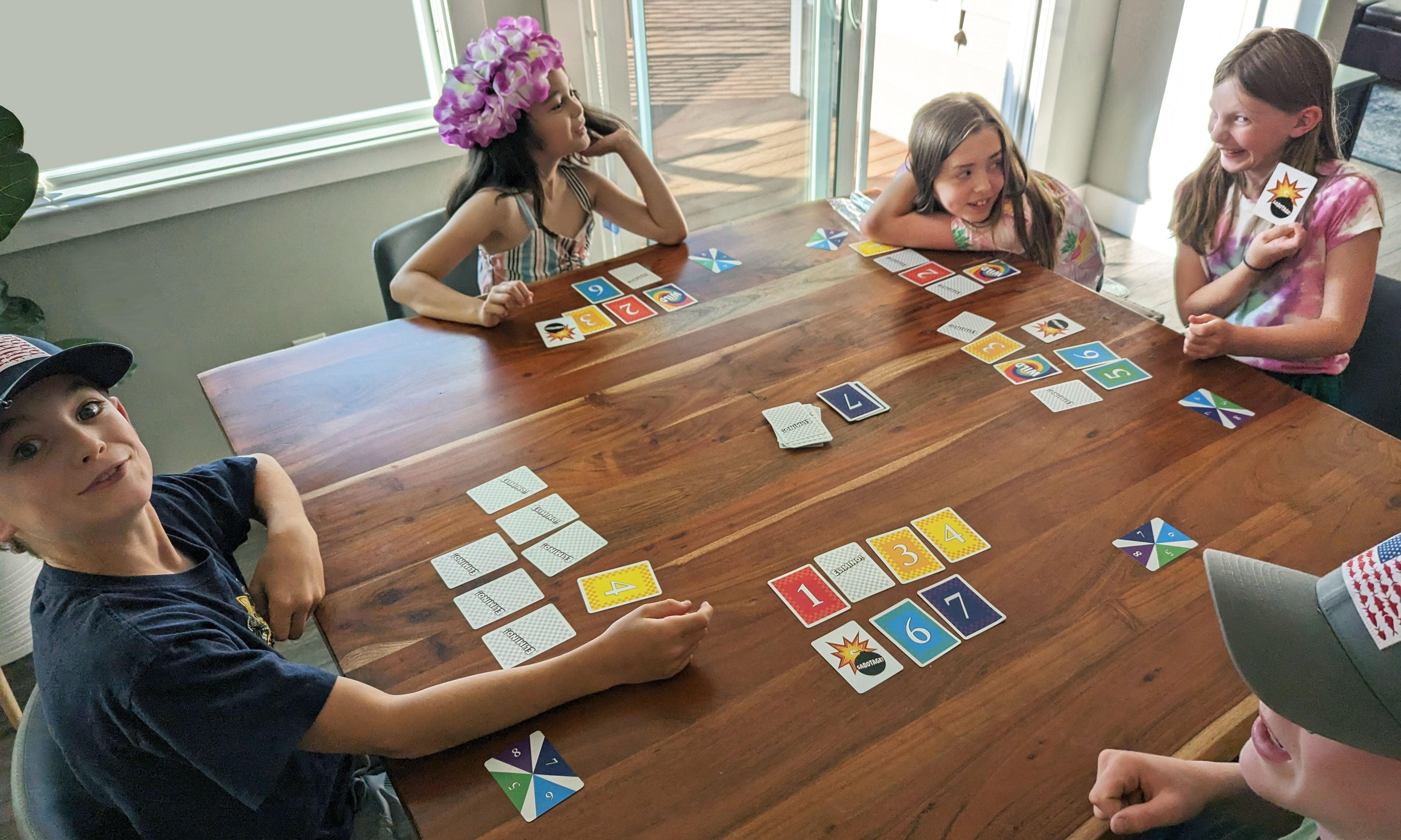 Kids playing Elimino around a table with young girl holding a sabotage card
