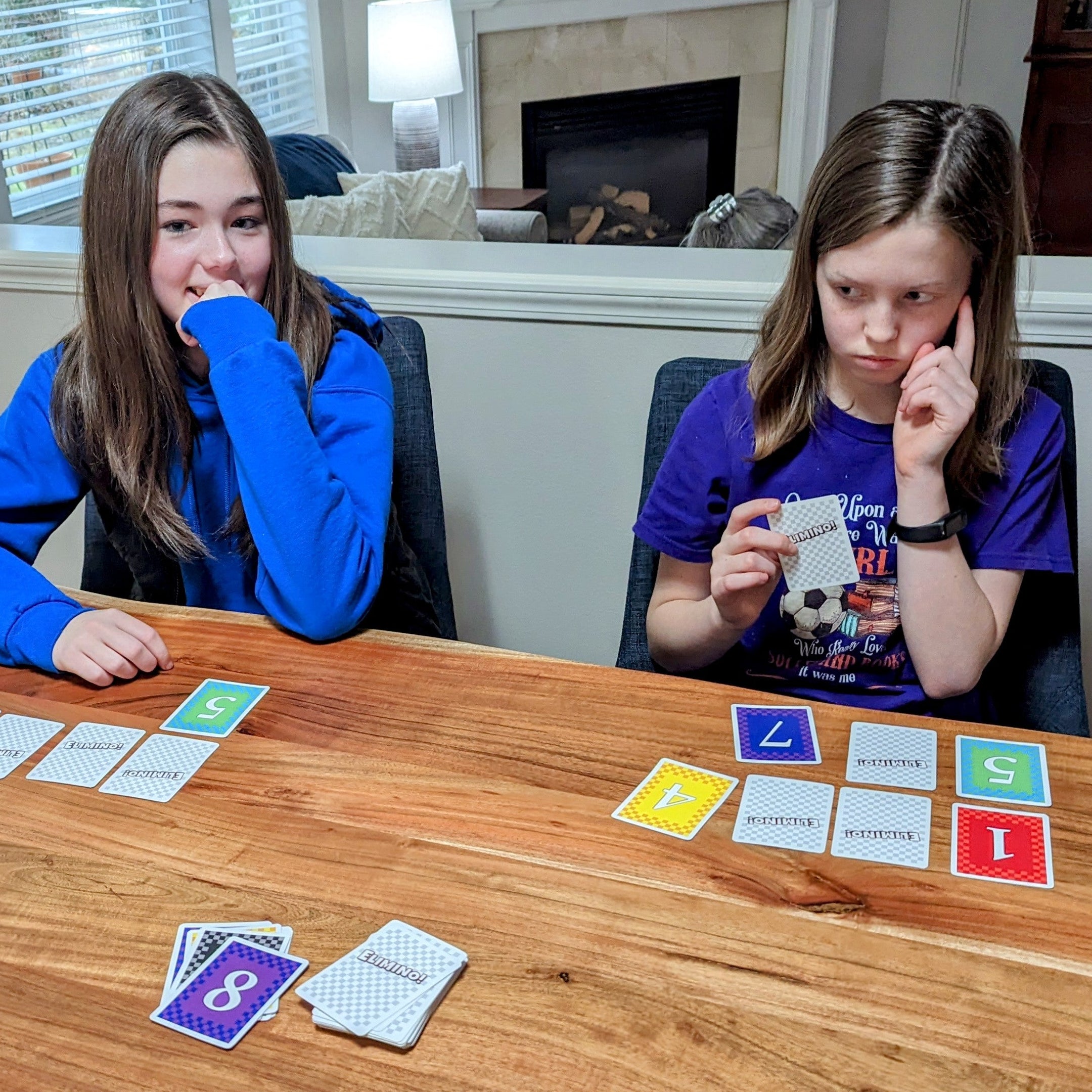 Two children playing a card game at a wooden table in a living room.