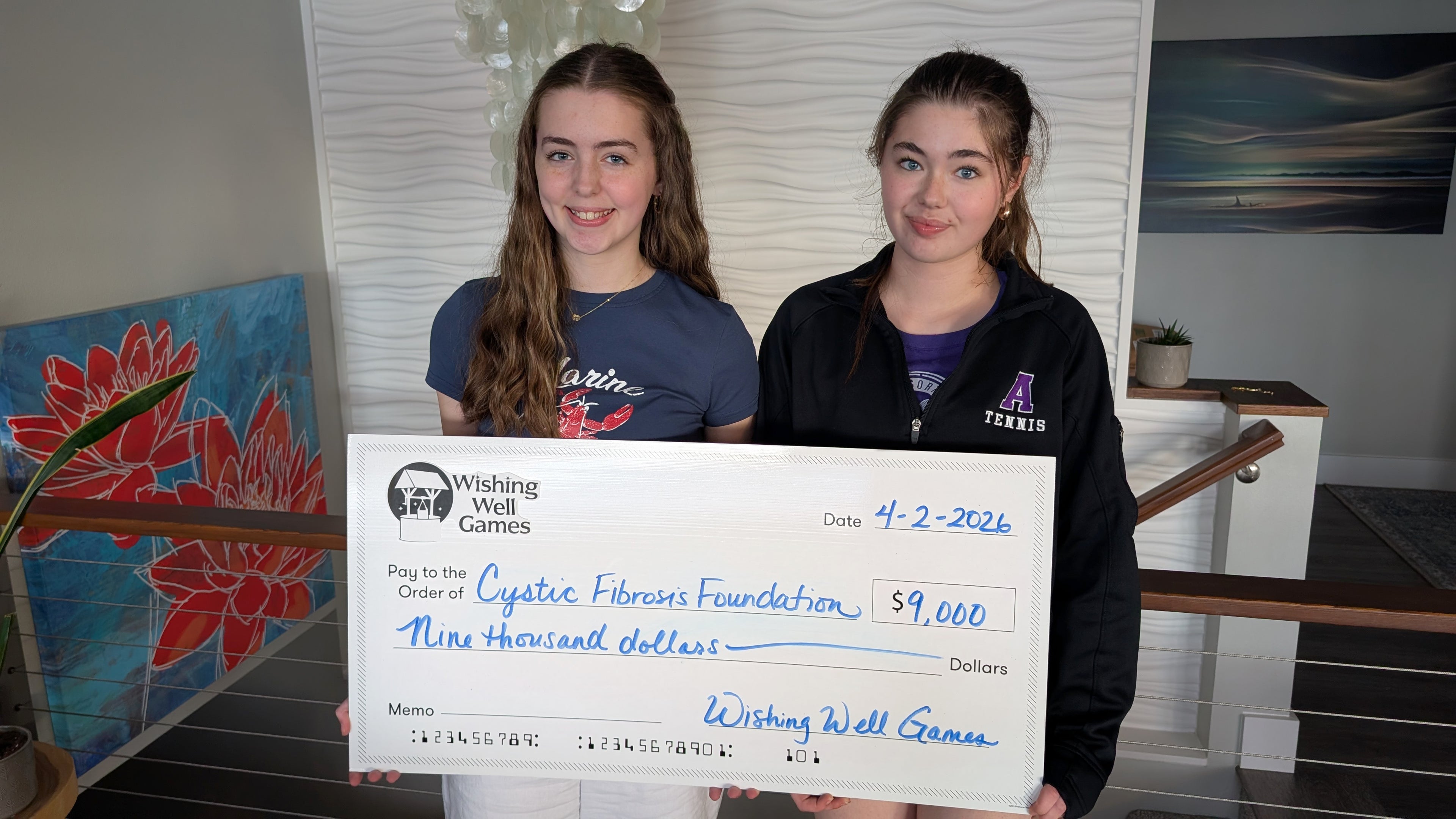 Two girls holding a large check for $9,000 from Wishing Well Games for the Cystic Fibrosis Foundation.