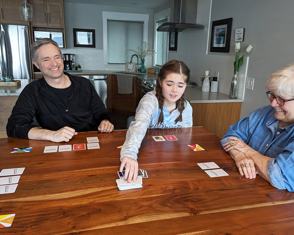 A young girl, father, and grandmother playing Elimino at a table
