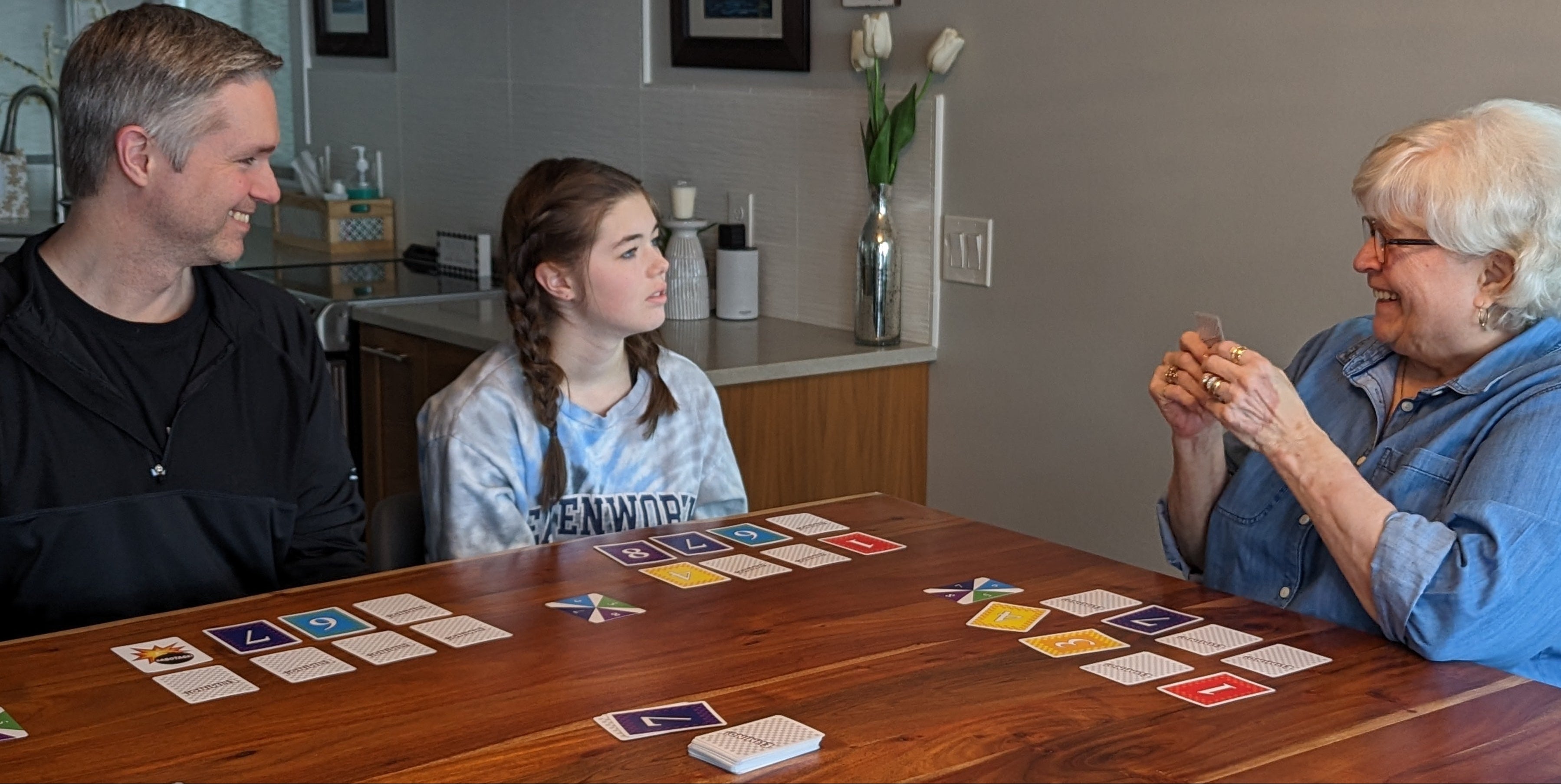 A girl sits at a table with her dad and grandma playing Elimino